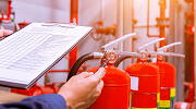 A worker holds a clipboard while inspecting several fire extinguishers