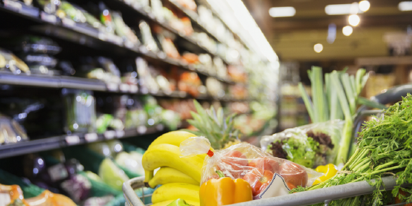 A grocery cart full of fruits and vegetables in a grocery store aisle. 