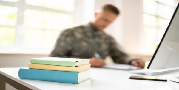 Man in military uniform seated at a desk with notebooks, textbooks and a computer.