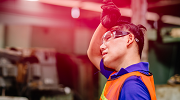 A worker wearing a visibility vest and safety goggles wipes his brow. 