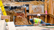 A construction worker stands inside a properly shored trench. 