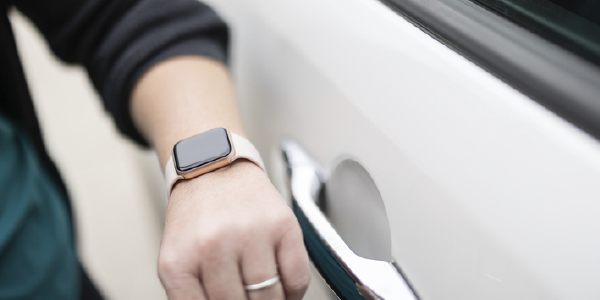 Outside a parked car, a woman checks her watch.