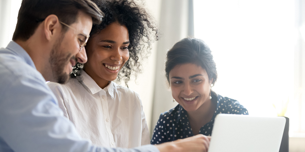 Three professionally dressed workers look at a laptop screen together.