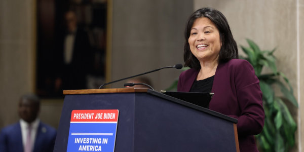 Acting Secretary of Labor Julie Su smiles as she speaks from a podium with a poster reading âPresident Joe Biden: Investing in Americaâ