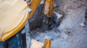 An excavator digs a hole, breaking street asphalt. 