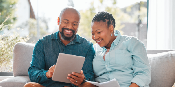 A Black man and woman, both in their 50s, smile as they read a tablet. 