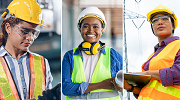 Three diverse women construction workers wearing a variety of protective gear, such as hardhats, ear protection, safety goggles, high-visibility vests and gloves.