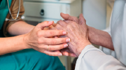 Close-up of medical professional in scrubs holding the hands of an elderly patient. 