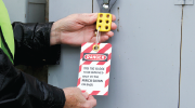 A person in a security vest locks and tags equipment to prevent it from starting up. 