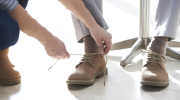 Close-up of a person crouching to tie the laces of an older person's shoes.