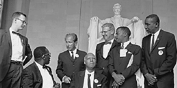 Black-and-white photo of seven March on Washington leaders including A. Philip Randolph and John Lewis in front of the Lincoln Memorial. 