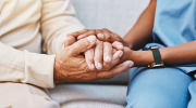 A close-up of two people holding hands. One is wearing medical scrubs.