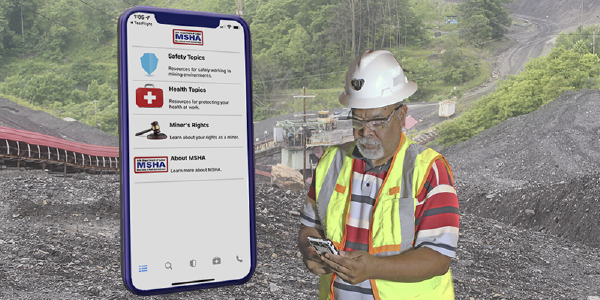 A man in a hardhat and safety vest checks his phone at an above-ground mine site. A cellphone, superimposed, shows the interface of the mine safety app.