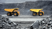 Two large dump trucks in an above-ground mining location, with dark rocks in the background and foreground.