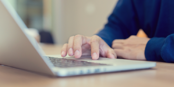 Close-up of a man's hands scrolling on a laptop.