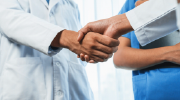 Close-up of medical professionals in scrubs and medical jackets shaking hands.