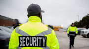 Two security officers in visibility jackets stroll through a parking lot on a cloudy day.