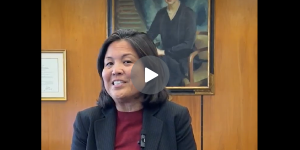 Screen grab of Acting Secretary Su speaking in her office, with a play button superimposed. 