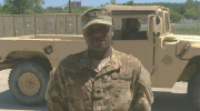 A man poses in front of an Army truck while in his military uniform.