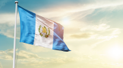 A Guatemalan flag flowing in the wind with a sunset background.