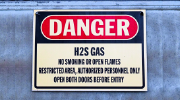 Sign on a wall reads: Danger, H2S gas, no smoking or open flames, restricted area, authorized personnel only, open both doors before exit.