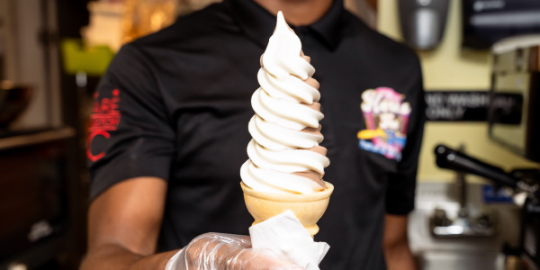 An ice cream parlor worker holds out a cone of chocolate-and-vanilla swirl soft serve.