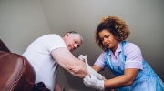 A caregiver places a compression sleeve on the arm of an older man who is seated in an armchair.