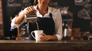 A barista in an apron pours milk into a mug.