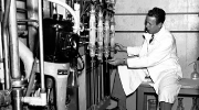 Black and white photo of a 1950s worker wearing a lab coat but no other protective gear working with complicated machinery. Credit: U.S. Energy Department