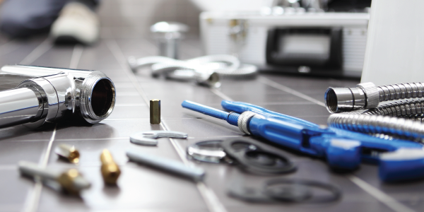 Plumbing equipment lies scattered on the tiled floor of a bathroom. 