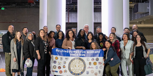 Acting Secretary Su and dozens of workers smile behind a banner reading "Building power for workers since 1896"