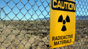 A sign on a fence in the desert reads: Caution, radioactive materials