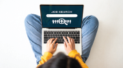 A woman scrolls through a laptop opened to a screen that reads "Job Search."