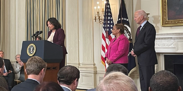 Acting Secretary Su speaks at a podium in the White House while President Biden looks on. 