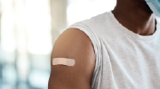 A man in a tee shirt has the sleeve rolled up and a band-aid on his upper arm, covering the site of a recent shot. 