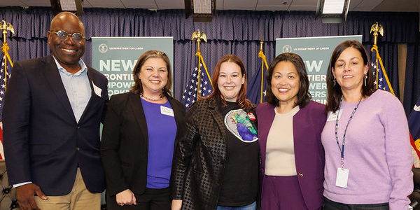 Acting Secretary Su host poses with four panel members in front of signs reading New Frontiers for Empowering Workers & Business.