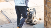 A man pushes a power tool over a concrete patio.