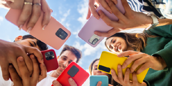 Shot from below, six young people stare at the screens of their brightly colored phones.