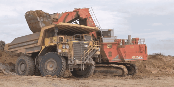 An excavator empties its bucket into a giant dump truck at a surface mine.