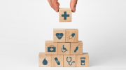 Wooden blocks stacked in a pyramid. Each is decorated with an icon suggesting some aspect of health care â a medical cross, an EKG heart, a pill, a medical bag, a handicap icon, a syringe, a blood droplet, a bandage, a stethoscope and a prescription bottl