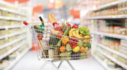 A shopping cart filled with fruits and vegetables in a grocery store aisle. 