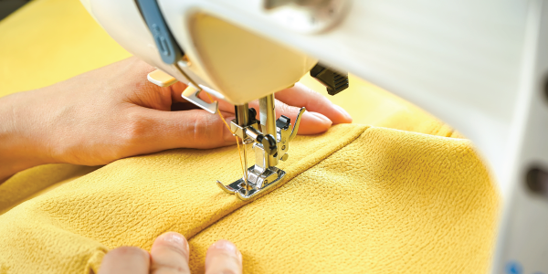 Close-up of a womans hands sewing yellow fabric with a sewing machine.