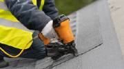 A roofer applies roofing tiles with a nail gun.