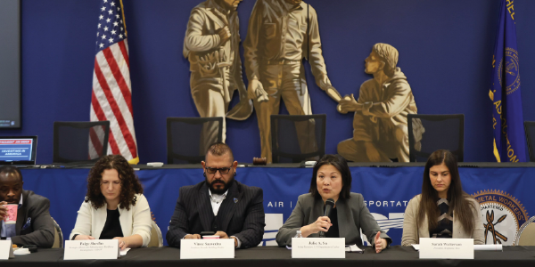 Acting Secretary Su speaks into a microphone while on a panel with four other men and women.