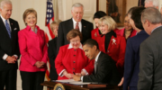 Historic photo shows President Obama signing the Lilly Ledbetter Fair Pay Act in the White House, as Joe Biden, Lilly Ledbetter and others look on. 