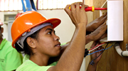 A woman wearing an orange hard hat works on an electrical box in Timor-Leste. Photo: UN Women/Betsy Davis.