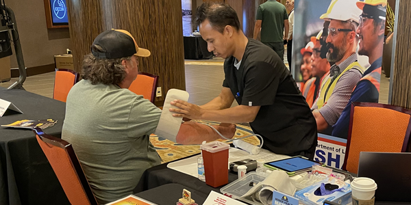 A medical professional puts a blood pressure cuff on a miner at a booth during a free health clinic event.