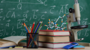 A desk with books and a microscope in front of a chalkboard with math equations 