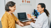 An audiologist speaks with an older female patient in a medical office. 