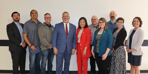 Acting Secretary Su and Secretary Cardona smile for a photo with several other adults in a school building.